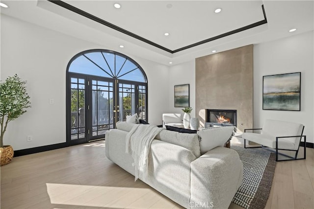 living area featuring light wood-style flooring, french doors, baseboards, a fireplace, and a raised ceiling