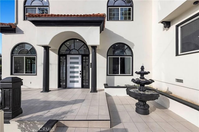 property entrance featuring stucco siding, a tiled roof, and a patio