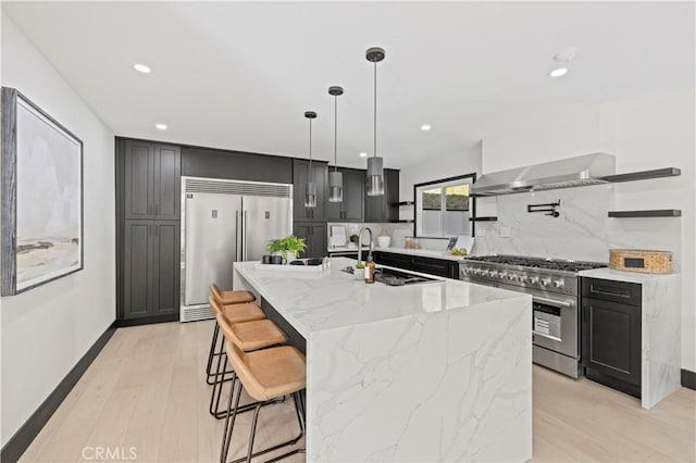 kitchen with a sink, tasteful backsplash, wall chimney exhaust hood, light stone countertops, and high end appliances