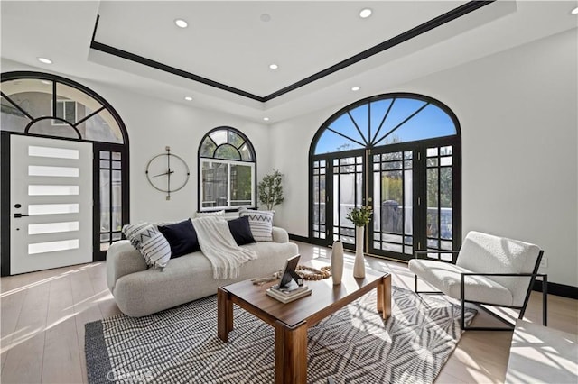 living area featuring french doors, a raised ceiling, light wood-style floors, and baseboards