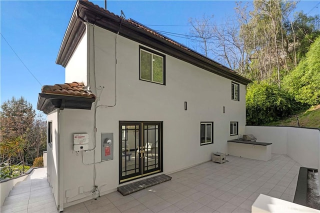 rear view of property with stucco siding, a tiled roof, and a patio