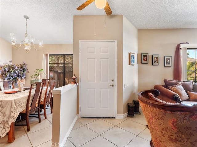 entrance foyer with light tile patterned floors, ceiling fan with notable chandelier, and a textured ceiling