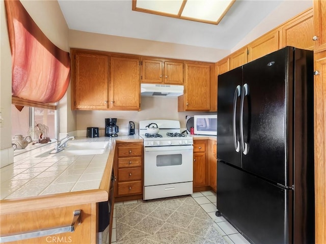 kitchen featuring white appliances, a sink, tile counters, under cabinet range hood, and brown cabinets