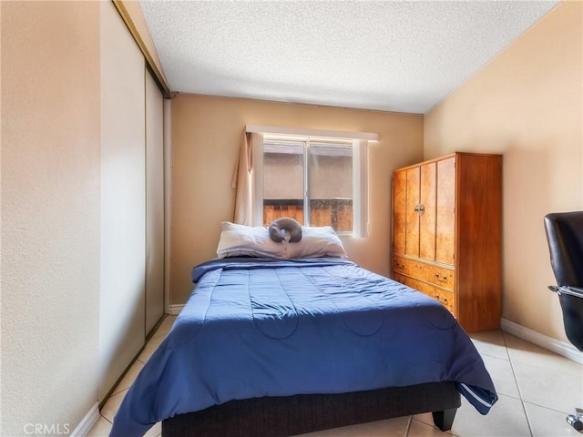 bedroom featuring light tile patterned floors, a textured ceiling, and baseboards