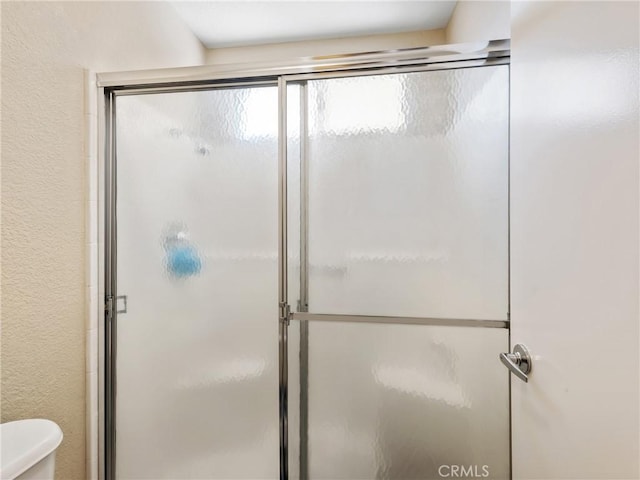 bathroom featuring toilet, a stall shower, and a textured wall