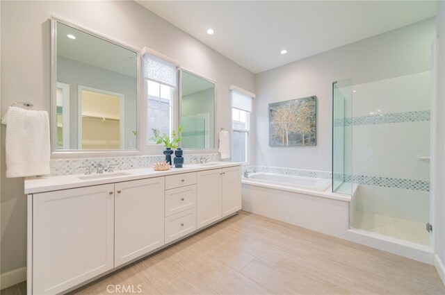 bathroom featuring a bath, a shower stall, double vanity, and a sink