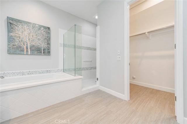 bathroom featuring a spacious closet, baseboards, a garden tub, a stall shower, and wood finished floors