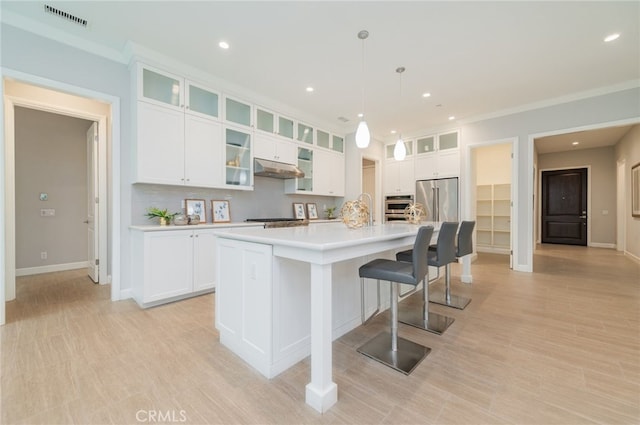 kitchen featuring visible vents, a large island, under cabinet range hood, white cabinetry, and stainless steel appliances