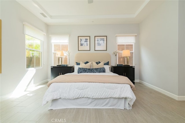 bedroom with a tray ceiling, baseboards, visible vents, and light wood-style flooring