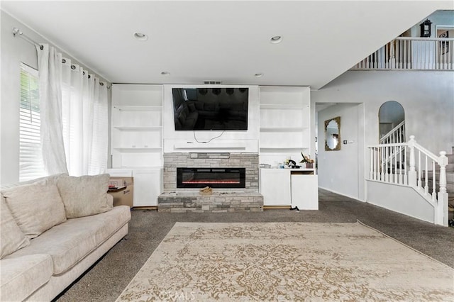 living room featuring built in features, stairway, a stone fireplace, and carpet floors