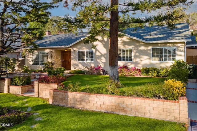 ranch-style home featuring stucco siding, a chimney, a front yard, and roof with shingles