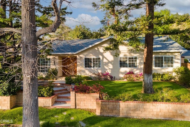 ranch-style home with stucco siding, roof with shingles, and a front lawn