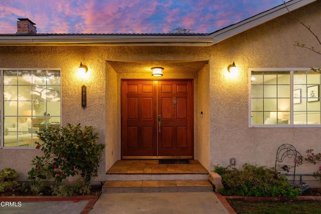 exterior entry at dusk featuring a chimney and stucco siding