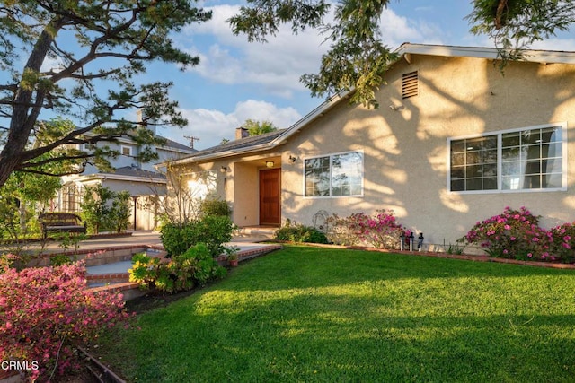 view of front of house with stucco siding, a chimney, and a front yard