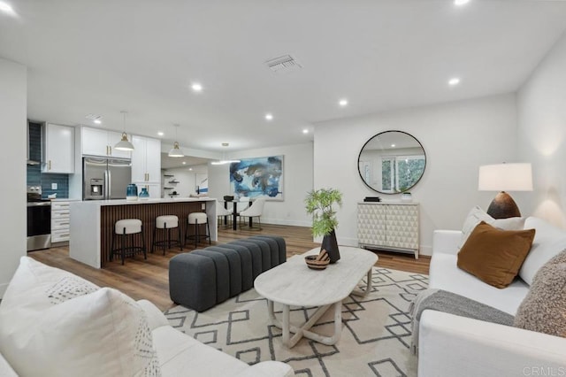 living area with light wood finished floors, visible vents, recessed lighting, and baseboards