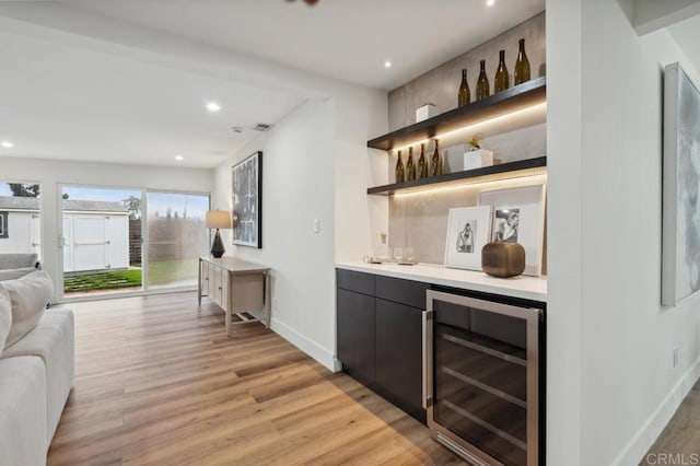 bar featuring light wood-type flooring, recessed lighting, wine cooler, a bar, and baseboards