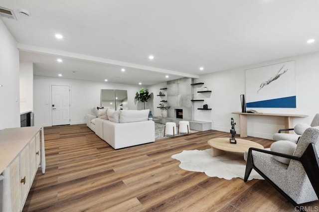 living room featuring a tiled fireplace, recessed lighting, and wood finished floors