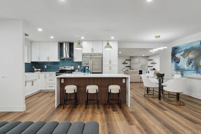 kitchen featuring stainless steel appliances, wall chimney exhaust hood, a center island, and light wood finished floors