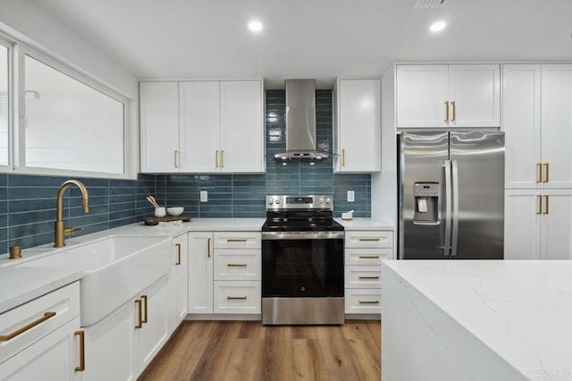 kitchen with a sink, appliances with stainless steel finishes, wall chimney exhaust hood, and white cabinetry