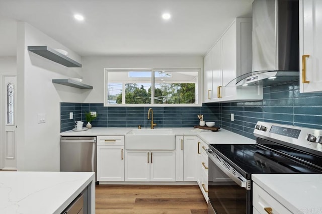 kitchen featuring a sink, light stone counters, stainless steel appliances, light wood-style floors, and wall chimney exhaust hood