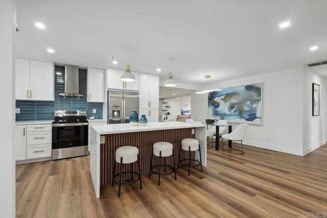 kitchen with light countertops, stainless steel appliances, wood finished floors, white cabinetry, and wall chimney exhaust hood