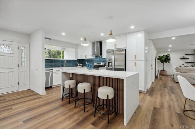 kitchen featuring white cabinets, appliances with stainless steel finishes, a center island, and wall chimney exhaust hood