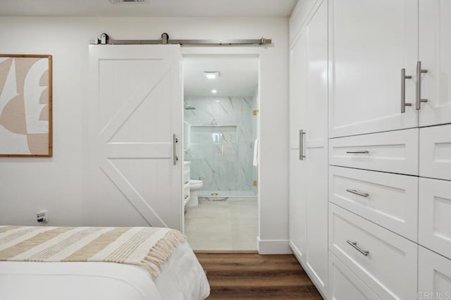 bedroom featuring a barn door, dark wood-style floors, visible vents, and ensuite bathroom