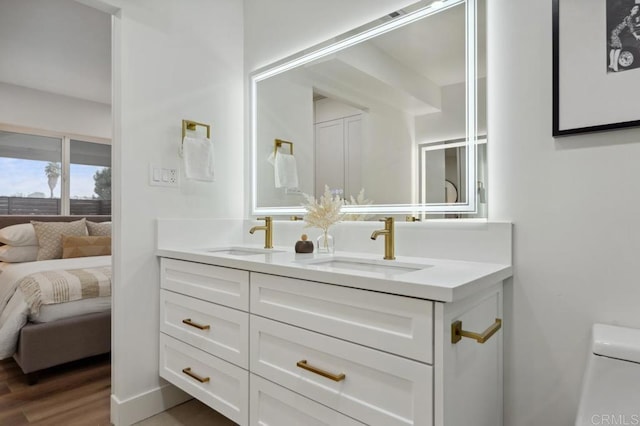 ensuite bathroom featuring double vanity, wood finished floors, toilet, and a sink