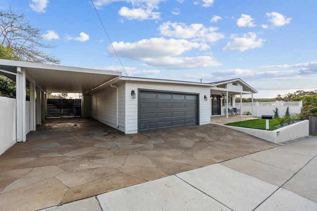 view of front of home with an attached carport, an attached garage, concrete driveway, and fence