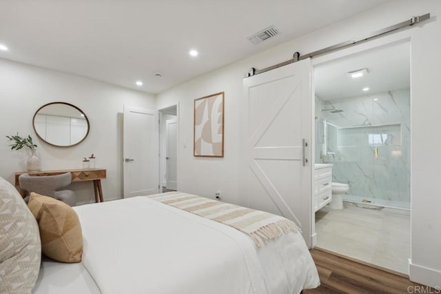 bedroom with wood finished floors, visible vents, recessed lighting, a barn door, and connected bathroom