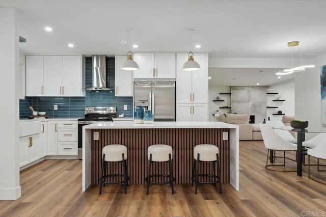 kitchen featuring a center island, stainless steel appliances, wall chimney exhaust hood, and light wood-style floors