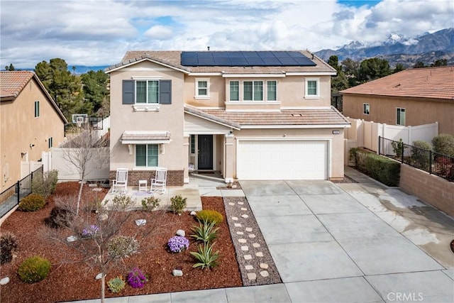 traditional home featuring stucco siding, driveway, roof mounted solar panels, fence, and a garage