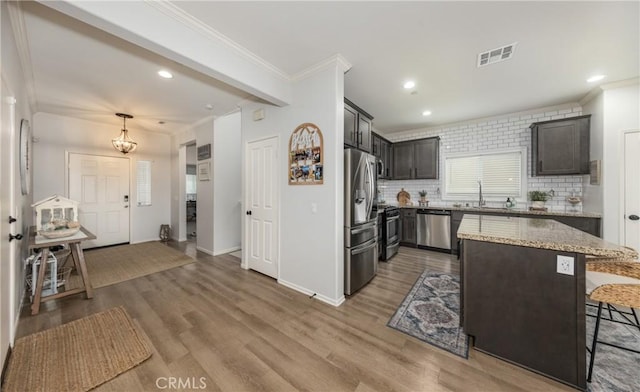 kitchen with light stone countertops, visible vents, a sink, appliances with stainless steel finishes, and crown molding