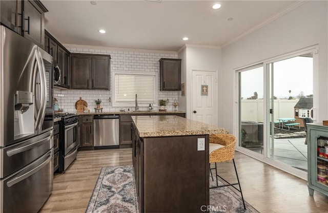 kitchen featuring dark brown cabinets, crown molding, light stone counters, appliances with stainless steel finishes, and a kitchen breakfast bar