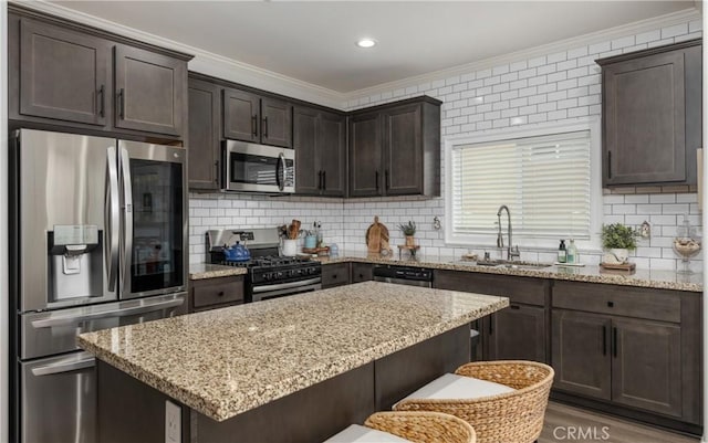 kitchen featuring dark brown cabinets, a center island, ornamental molding, appliances with stainless steel finishes, and a sink