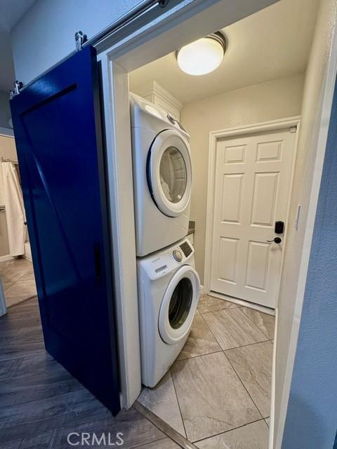 clothes washing area featuring laundry area, stacked washing maching and dryer, and a barn door