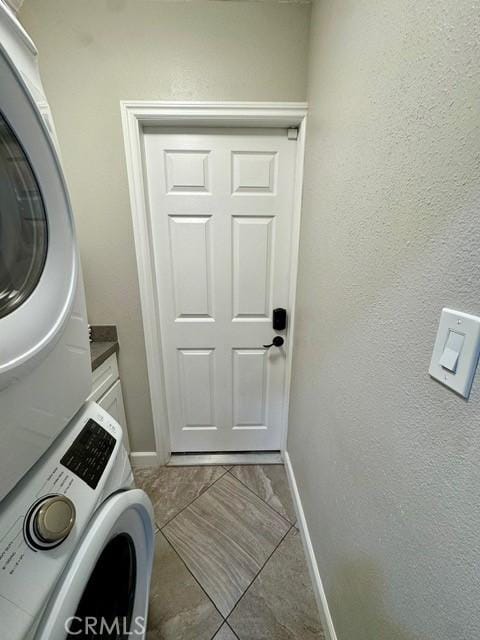 laundry area with baseboards, stacked washer / drying machine, and a textured wall