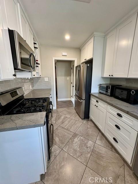 kitchen featuring light stone countertops, a toaster, stainless steel appliances, white cabinets, and tasteful backsplash