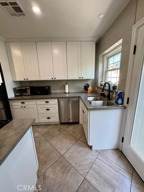 kitchen with visible vents, a sink, stainless steel dishwasher, white cabinets, and decorative backsplash