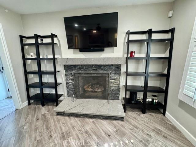 living room with a stone fireplace, baseboards, and wood finished floors