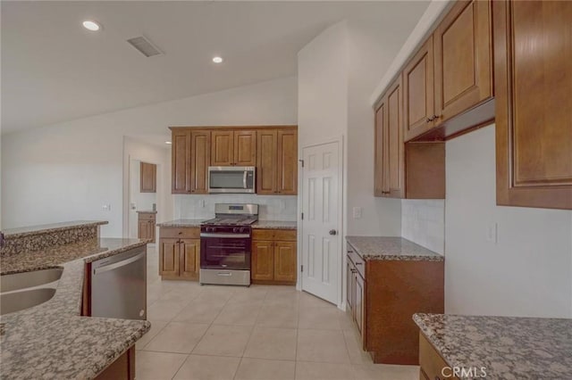 kitchen with brown cabinets, a sink, appliances with stainless steel finishes, lofted ceiling, and light stone countertops