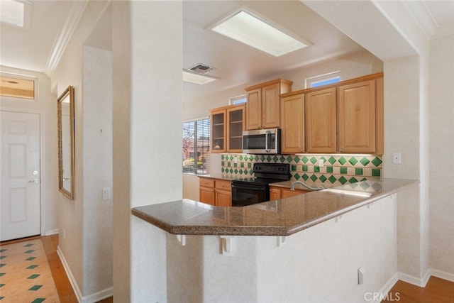 kitchen with electric range, visible vents, stainless steel microwave, a kitchen breakfast bar, and decorative backsplash