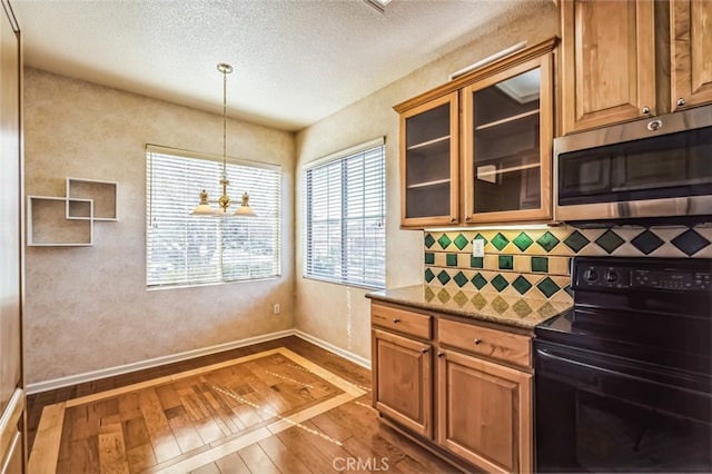 kitchen with stainless steel microwave, glass insert cabinets, decorative backsplash, hardwood / wood-style flooring, and black electric range oven