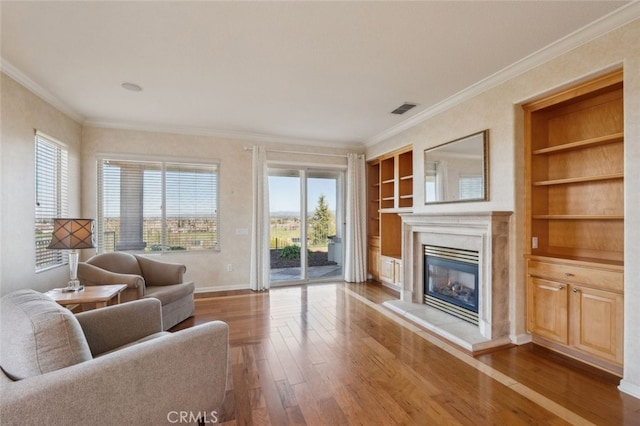 living area with built in features, ornamental molding, a glass covered fireplace, and hardwood / wood-style flooring