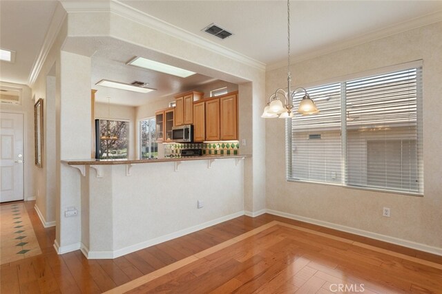 kitchen with visible vents, a breakfast bar, an inviting chandelier, light wood-style floors, and stainless steel microwave