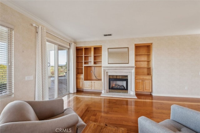 living area featuring visible vents, baseboards, built in features, wood finished floors, and a glass covered fireplace