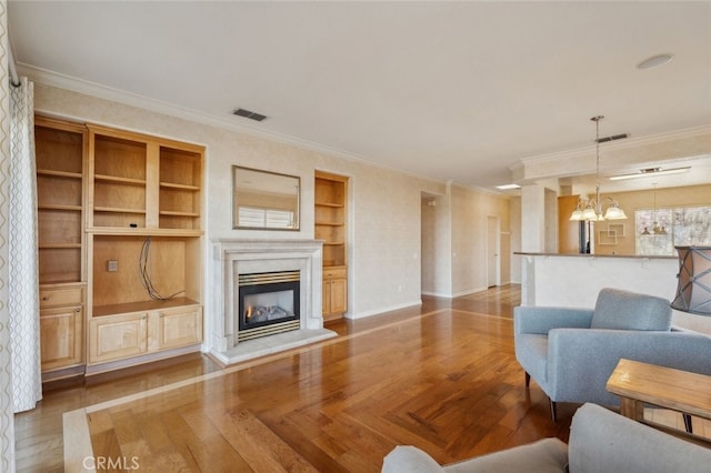 living area with built in features, visible vents, an inviting chandelier, and a glass covered fireplace