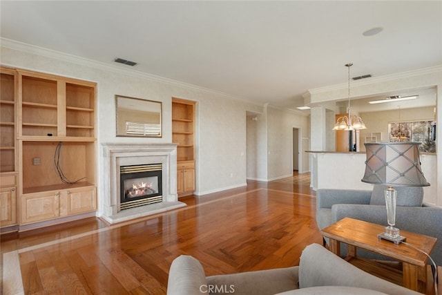 living room featuring a notable chandelier, wood finished floors, visible vents, and a glass covered fireplace