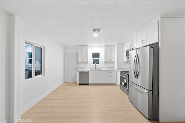 kitchen with light wood finished floors, visible vents, appliances with stainless steel finishes, white cabinetry, and a sink