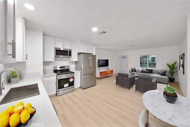 kitchen featuring visible vents, a sink, stainless steel appliances, light countertops, and white cabinetry